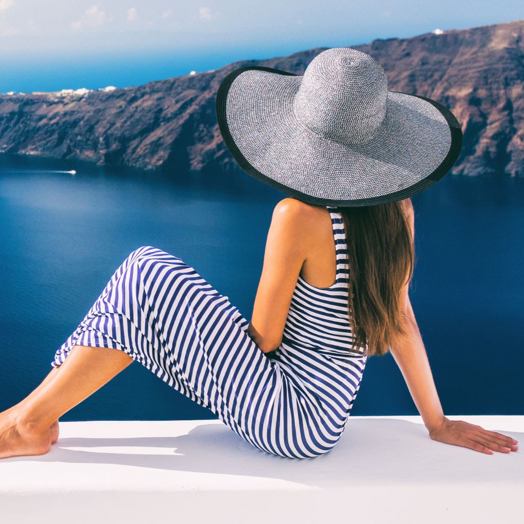 Photo d'une femme portant un chapeau assise en biais de dos sur un mur admirant le paysage